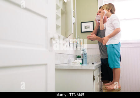 Padre e figlio l'applicazione di crema di rasatura sulla faccia nella stanza da bagno Foto Stock