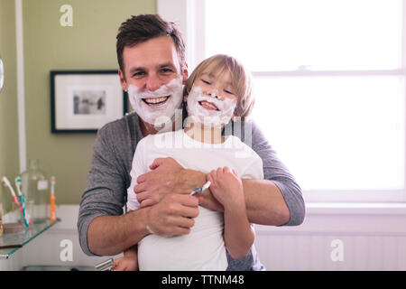 Ritratto di felice padre e figlio con crema di rasatura sulla faccia in piedi in bagno Foto Stock