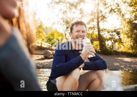 Ritratto di uomo acqua potabile mentre è seduto con la donna sul molo Foto Stock