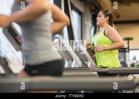 Sezione mediana della donna con un amico che esercitano sul tapis roulant in palestra Foto Stock