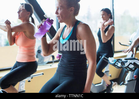 Donne stretching mani mentre è seduto sulla cyclette in palestra Foto Stock