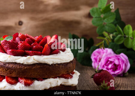 Crema di burro fatti in casa torta con fragole, festosa tabella con le rose rosa e bacche, rustico sfondo di legno Foto Stock