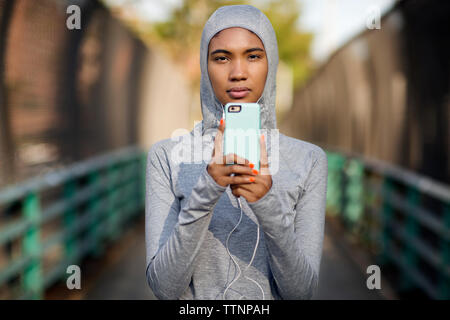 Ritratto di donna che indossa maglietta con cappuccio mentre utilizzando smart phone sul sentiero Foto Stock