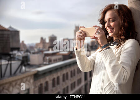 Donna sorridente fotografare con smart phone sul balcone Foto Stock