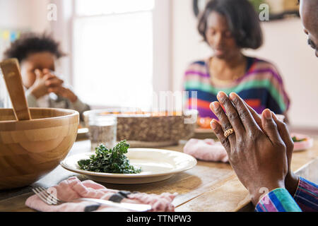 Immagine ritagliata della famiglia dire grazia al tavolo da pranzo Foto Stock