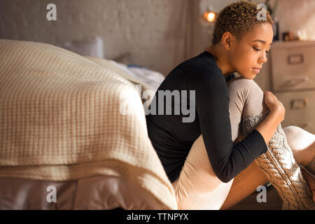 Vista laterale del triste donna seduta sul pavimento in camera da letto Foto Stock