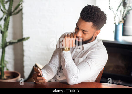 Giovane uomo utilizzando smart phone seduti a tavola Foto Stock