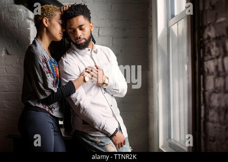 Rilassata coppia giovane con gli occhi chiusi in piedi dalla finestra a casa Foto Stock