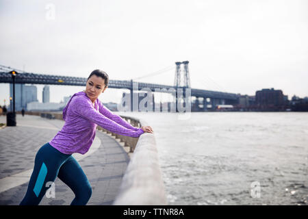 Vista laterale del determinato atleta femminile che esercitano sul sentiero con Williamsburg Bridge in background Foto Stock