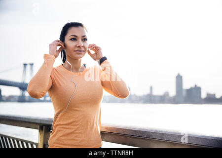 Sportivo da donna che indossa gli auricolari dal fiume con Williamsburg Bridge in background Foto Stock