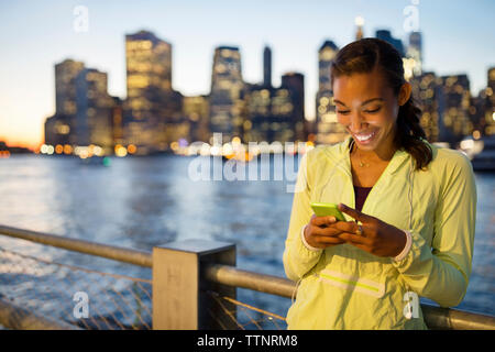Donna felice usando il cellulare mentre in piedi dal fiume Foto Stock