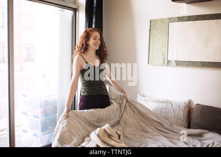 Donna sorridente rendendo letto a casa Foto Stock