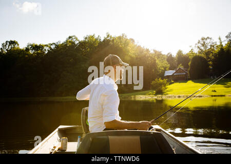 L'uomo la pesca mentre sedendo nel canotto sul lago durante la giornata di sole Foto Stock