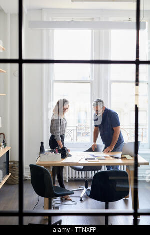 uomo d'affari che discute con una collega donna nell'ufficio creativo visto dalla finestra Foto Stock