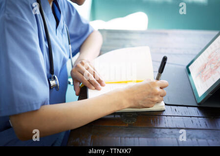Sezione mediana del medico donna scrivendo sul diario mentre si lavora alla scrivania in ospedale Foto Stock