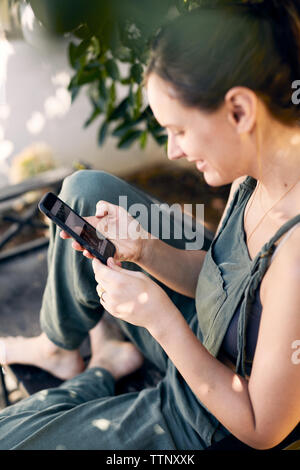 Elevato angolo di visione della donna che utilizza internet sul telefono nel cortile posteriore Foto Stock