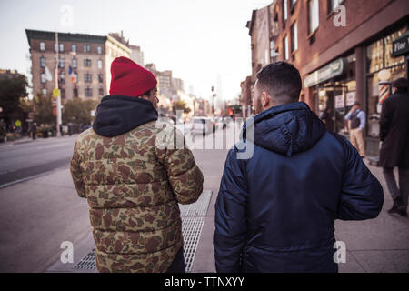 Vista posteriore di amici camminando sul sentiero in mezzo di edifici Foto Stock