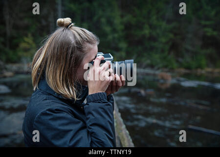 Vista laterale della donna fotografare con fotocamera contro fiume Foto Stock