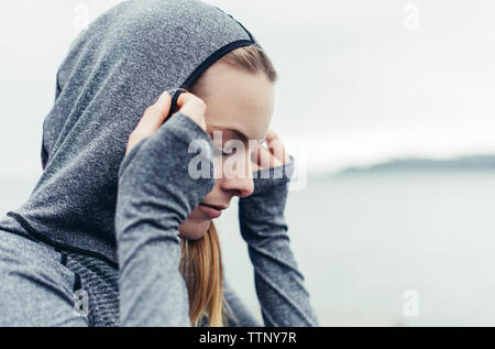 Close-up di bella atleta femminile indossando giacca con cappuccio contro il cielo chiaro Foto Stock