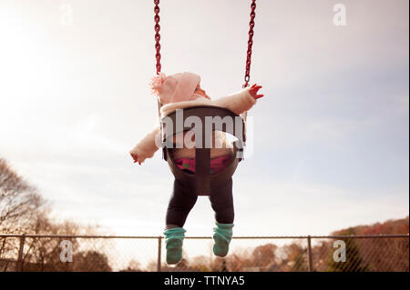 Basso angolo vista della bambina seduta su swing in posizione di parcheggio Foto Stock