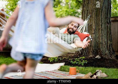 Sezione bassa della figlia che corre verso il padre relax su amaca in cantiere Foto Stock