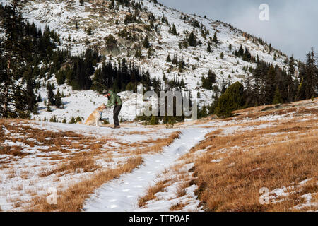 Uomo felice strofinarsi il cane mentre si sta in piedi sul campo durante il periodo invernale Foto Stock