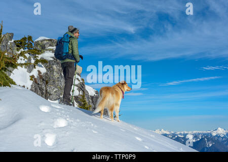 Escursionista maschio e cane sulla cima della montagna nella neve Foto Stock