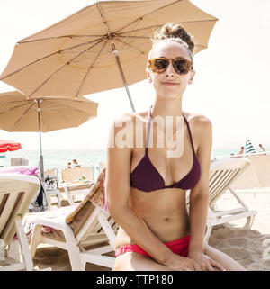 Donna in bikini seduto sulla sedia a sdraio in spiaggia Foto Stock