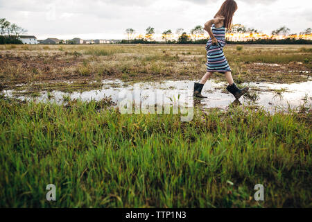 Vista laterale del disordine ragazza camminare sul campo umido Foto Stock