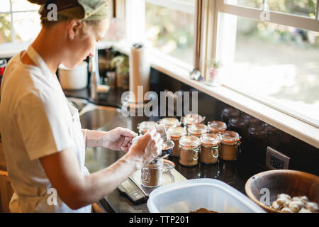 Donna di spezie di riempimento in vasetti di vetro mentre si sta in piedi in cucina Foto Stock