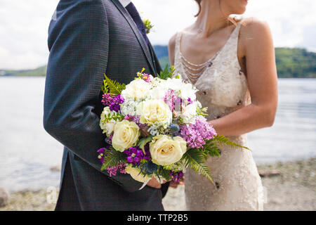 Sezione mediana della sposa giovane azienda bouquet mentre in piedi sul lungolago Foto Stock