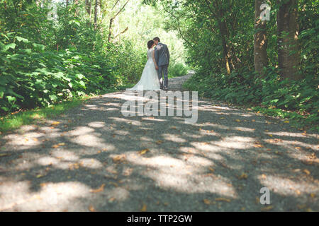 Sposa giovane kissing mentre permanente sulla strada da piante in foresta Foto Stock