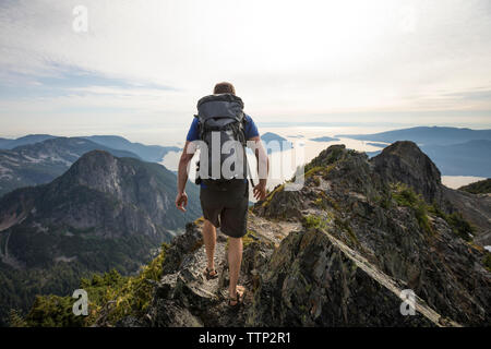 Vista posteriore di un escursionista con zaino camminando sulla montagna contro sky Foto Stock