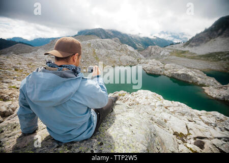 Vista posteriore di un escursionista fotografare mentre è seduto sulla scogliera a Garibaldi Provincial Park Foto Stock
