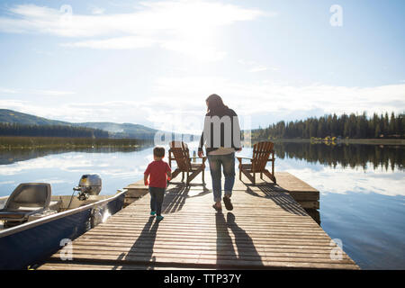 Vista posteriore di madre e figlio camminando sul molo in legno sopra il lago contro sky Foto Stock