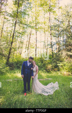 Sposa giovane in piedi sul campo erboso contro gli alberi nelle foreste Foto Stock