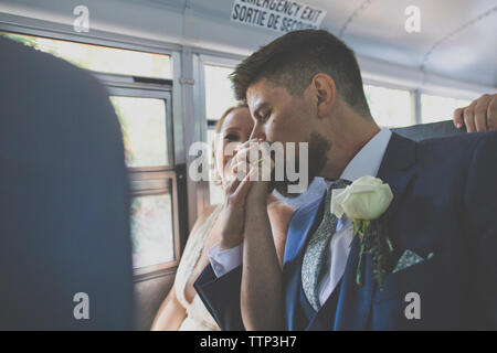 Il marito baciare sposa sposa la mano mentre è seduto in bus durante la cerimonia nuziale Foto Stock