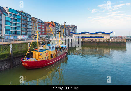 Barca da pesca nel porto di Ostenda in città dalla passeggiata lungomare con il moderno mercato del pesce in background, Fiandre Occidentali, Belgio. Foto Stock