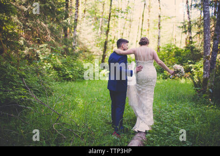 Vista posteriore della sposa giovane camminando sul campo erboso in foresta Foto Stock