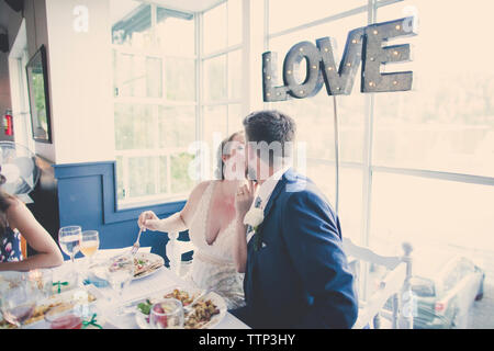 Sposa giovane kissing seduti nel ristorante alla cerimonia di nozze Foto Stock