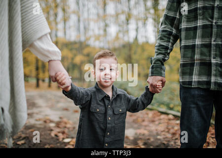 Ritratto di carino sorridente figlio di genitori tenendo le mani e piedi nel bosco durante la stagione autunnale Foto Stock