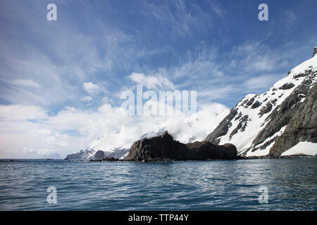 Mare e montagne coperte di neve contro il cielo nuvoloso Foto Stock