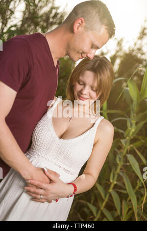 Amare luomo e felice donna incinta in estate il parco fiorito. Felice Coppia matura in amore abbracciando outdoor Foto Stock