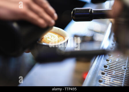 Ritagliate la mano del barista versando il latte nel caffè mentre Rendere spumoso drink presso il cafe Foto Stock