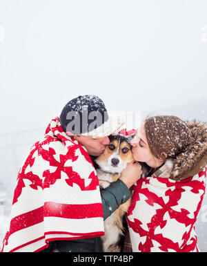 Giovane & cane huddle in coperta durante la nevicata & kiss dog insieme Foto Stock