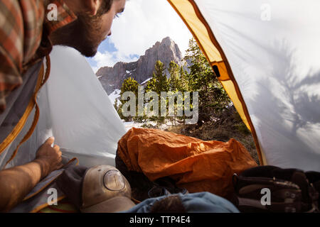 Uomo che guarda le montagne mentre è seduto in tenda Foto Stock