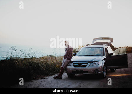 Ritratto di uomo appoggiato a vettura aperta sulla strada sterrata contro il cielo chiaro al Parco Nazionale di Yosemite Foto Stock