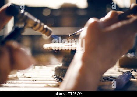 Immagine ritagliata di goldsmith utilizzando torcia soffiante in officina Foto Stock