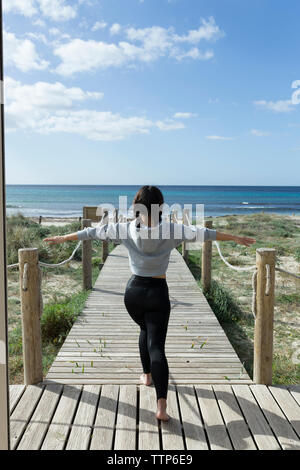 Vista posteriore della donna asiatica stiramento sulla passerella in legno Foto Stock