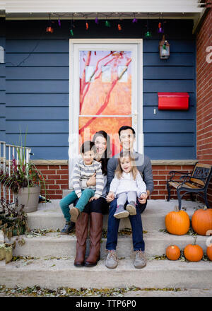 Ritratto di famiglia sorridente seduto sui gradini contro la casa durante il periodo di Halloween Foto Stock